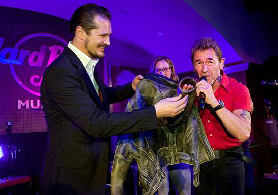 Foto unten vlnr: Marco Sellors (General Manager), Friederike Riedel (Sales Manager, beide Hard Rock Cafe München), Peter Maffay bei der Übergabe der grauen Lederjacke. c) Jens Hartmann